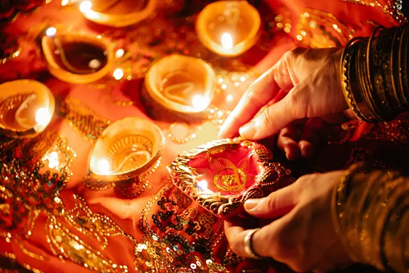 Hands lighting a diya lamp among golden bangles for Diwali.